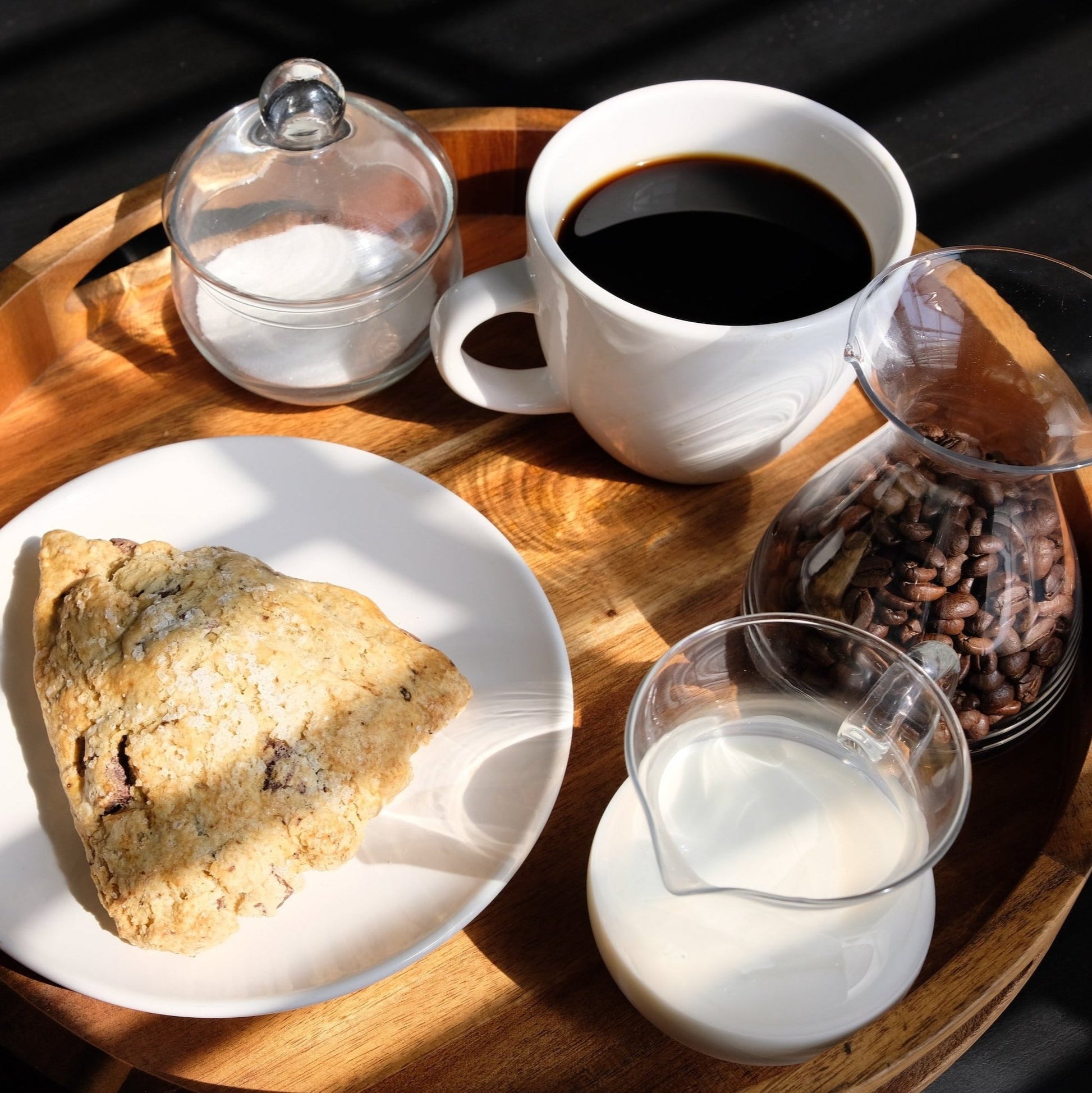 tray with coffee cup, small bottle of milk, plate with scone, and suger